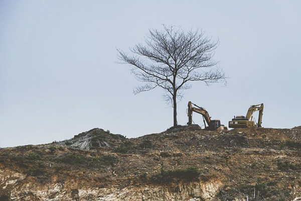 Diggers excavating on a hilly landscape.